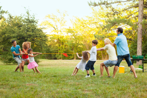 Two Families having fun playing tug of wars outdoors, after barbecue party. One Caucasian family and other mixed race family.