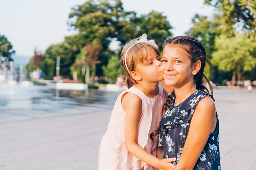 Cute little girl enjoying in a kiss by her older sister in the park.