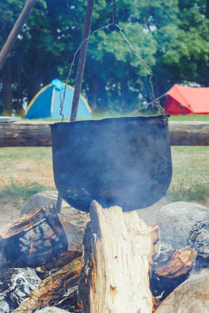 istock Steam from firewood surrounding cauldron with dish, cooking on campfire, hanging on tripod against camping tents. 1713582131