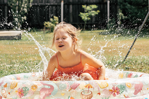 Little girl having fun splashing water in inflatable pool on summer day outside. Games and entertainment. Summer holidays. Happy childhood.Happy summer days. Positive emotions.