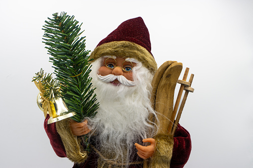 Santa Claus toy holding wooden skis  and a fir branch with a bell on a white background