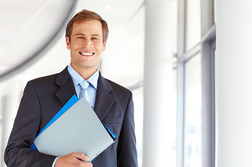 Portrait of handsome mid adult male business manager smiling while holding files. Horizontal shot.