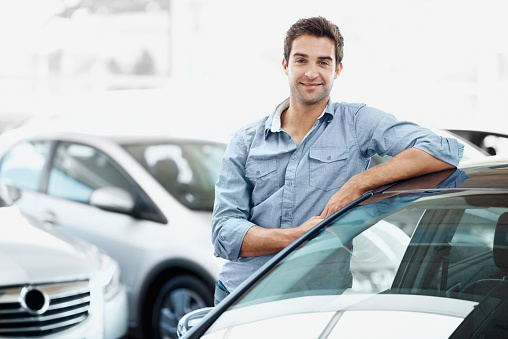 Smiling young guy standing alongside a car and leaning against it