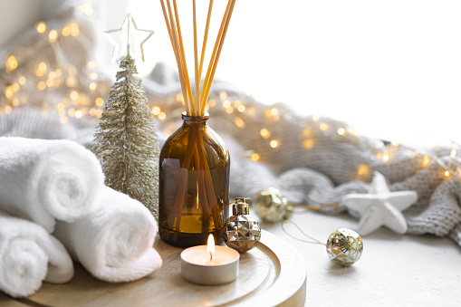 Christmas spa composition with towels, candle and incense sticks on a blurred background with bokeh lights.