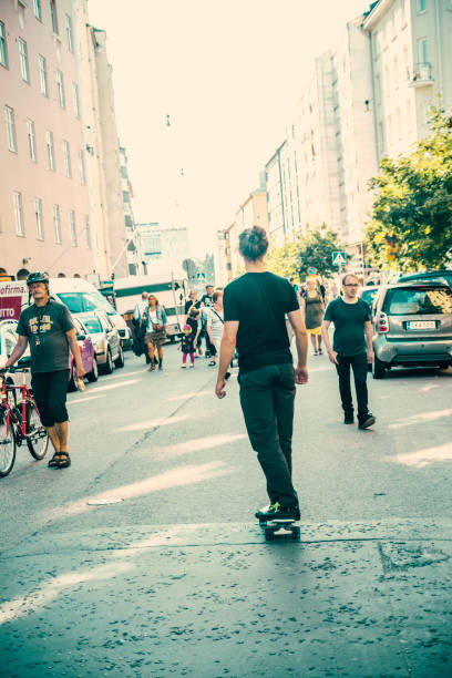 Rear view of man riding skateboard as the sun sets in the horizon. The man wears a cap and rides towards the sun.