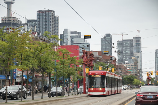 Toronto, Canada - August 24, 2023: A TTC 510 Spadina streetcar heads north past the red Gateway sculptures created by Millie Chen on Spadina Avenue near Dundas Street West. Overcast sky in the Kensington-Chinatown neighborhood downtown.