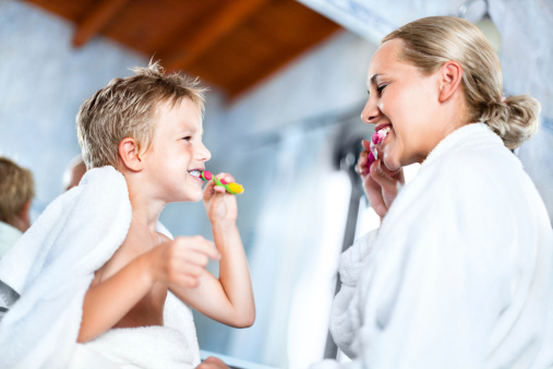 Little boy and his mother brushing teeth together in the bathroom.