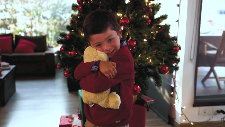 Happy little boy celebrating Christmas and hugging his new teddy bear very excited and lovingly