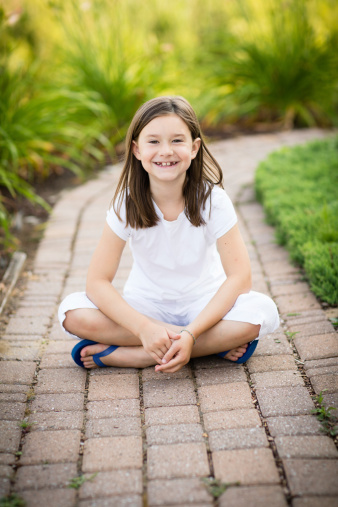 Color image of a happy, little girl, sitting outdoors on a sunny, summer day.