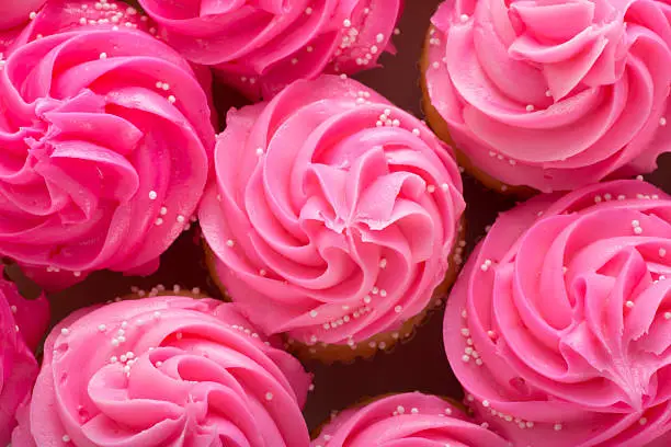 This is an overhead photo of cupcakes with pink icing and white sprinkles on top. The focus is on the cupcake in the middle.Click on the links below to view lightboxes.