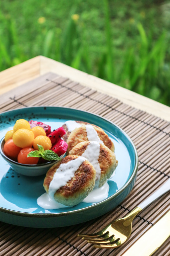 Vegan tofu cheese pancakes on blue plate with fresh tropical fruits and coconut cream closeup