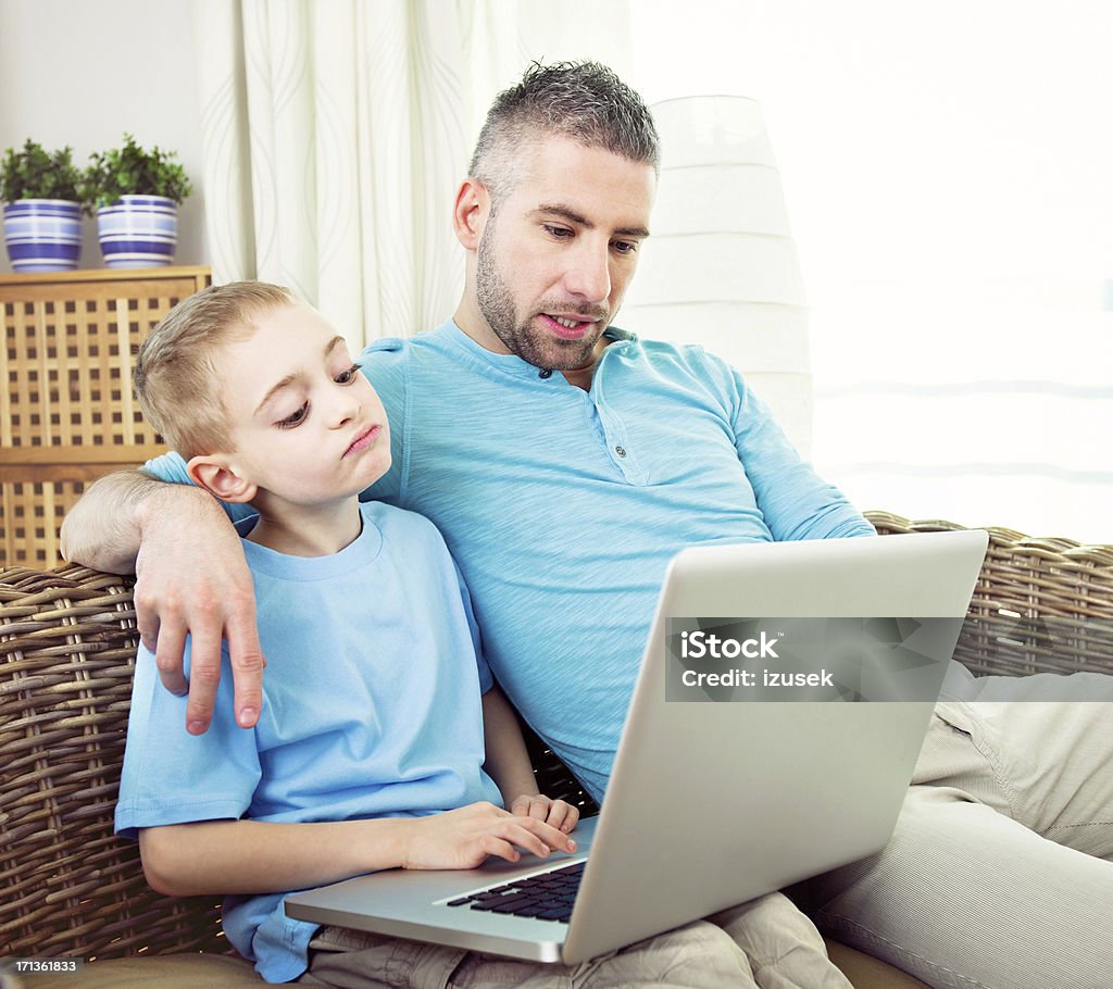 Happy Boy and Father with Laptop Computer Young boy sitting with his father on sofa at home and using laptop.  Boys Stock Photo