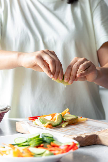 istock Woman preparing spring rolls in rice paper on kitchen table. 1713619798