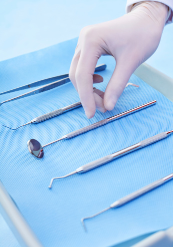 Close up of a tray with dental insturments and the dentist's hands picking up dental mirror.