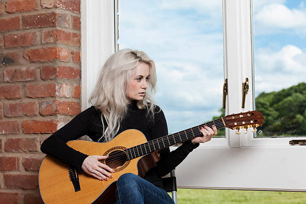 A young woman relaxes with her guitar beside a window.