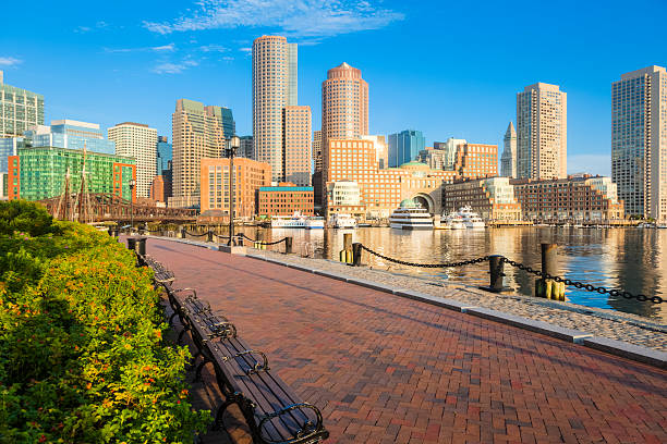 Boston Sunrise and Peaceful Setting along Fan Pier Downtown Boston's numerous skyscrapers are viewed from Fan Pier in the early morning under a beautiful blue sky. Park benches along with a red brick herringbone patterned walkway provide a peaceful place to enjoy the sights of the harbor. A thick nautical chain provides safety for those walking too close to the harbor's edge. HDR image. boston harbor stock pictures, royalty-free photos & images