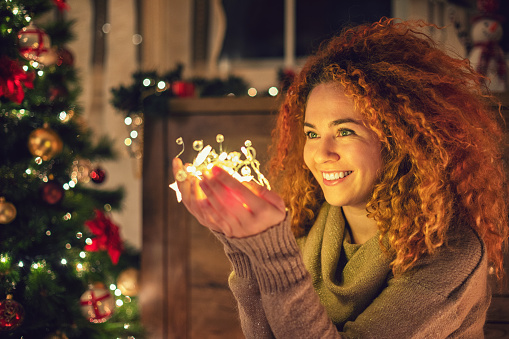 Young beautiful woman holding shiny Christmas lights