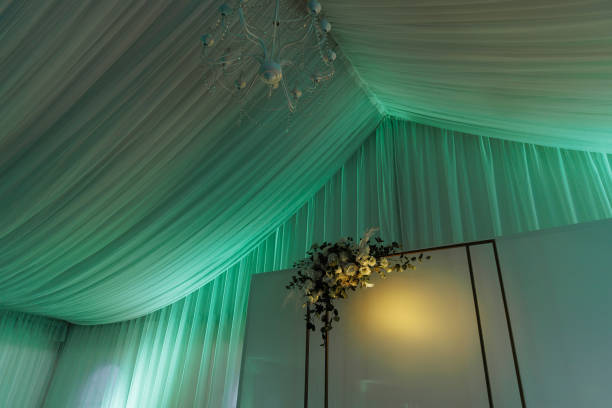Ceiling of a tent for a wedding celebration. Beautiful white interior with white draperies and colored lighting.