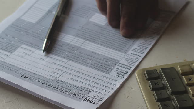 close-up of a man with a calculator and a pen filling out tax form 1040. selective focus. finance and taxes concept. residency and taxation.