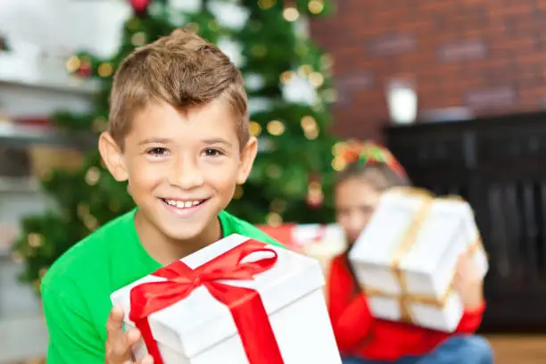 Photo of Smiling little boy opening Christmas presents with sister