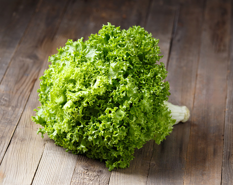 Big bunch of fresh green lettuce leaves on a wooden background. Healthy food, source of minerals and vitamins.