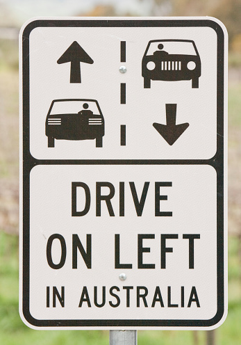 Reflective road sign advising visitors to drive on the left in Australia.