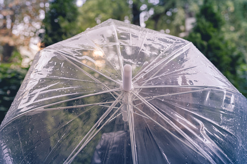 Autumn. Lonely sad redhead woman walking in a park, garden. View through wet  transparent umbrella with rain drops. Rainy day landscape. Vintage Toned