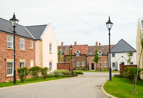 Brick houses and traditional landscaping on a quiet street in England in front of a gray sky.  The housing estate has old-fashioned streetlamps.