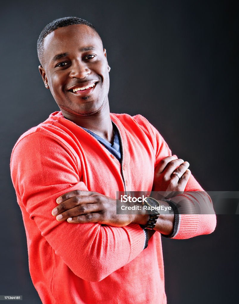 Half-length portrait of laughing man with folded arms against black "A young African-American man with his arms folded looks out, laughing, in this half-length portrait against a black background." 20-29 Years Stock Photo