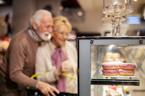 Selective focus on doughnuts at supermarket with senior couple in blurry background choosing pastry.