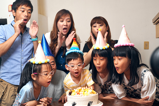 Multi-generation Asia family hold a birthday party to celebrate a boy’s birthday at home. A 5 years old boy blow out candles on his birthday party. They are wearing birthday hats and having fun together. It’s a happy theme about love concept, emotion, togetherness, life, enjoyment, Affectionate. There is father, mother, son, daughter, grandfather in this photo. There is a birthday cake on the table. The girl twins are indigenous in Taiwan.