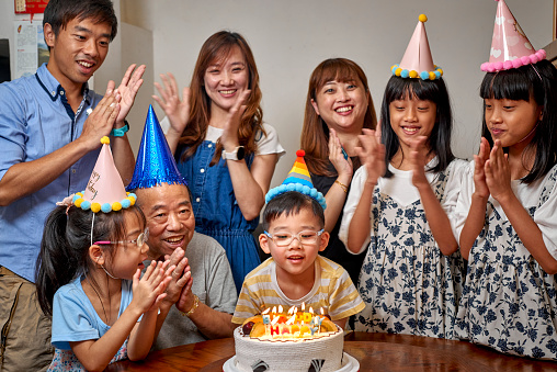 Multi-generation Asia family hold a birthday party to celebrate a boy’s birthday at home. All families sing a birthday song to the boy. They are wearing birthday hats and having fun together. It’s a happy theme about love concept, emotion, togetherness, life, enjoyment, Affectionate. There is father, mother, son, daughter, grandfather in this photo. There is a birthday cake on the table. The girl twins are indigenous in Taiwan.