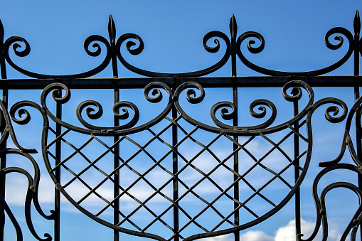 Fragment of black openwork wrought-iron fence grating against blue sky background. Close-up. Copy space.\tSelective focus.