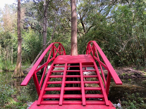 Image of Gorgeous fire engine red walking bridge onto green island over stream leading to pond and geese