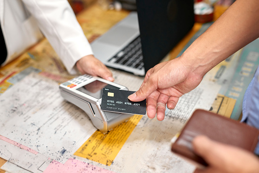 Female middle-aged pharmacist checkout with male customer in her pharmacy. The use wireless electronic payment with his credit card. Concept Pharmacist in the use of Medical.