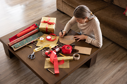 Latin American woman at home wrapping Christmas presents and writing a card - holiday concepts