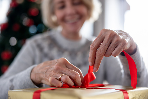 Close-up on a senior woman wrapping Christmas gifts and making a bow - holiday season concepts