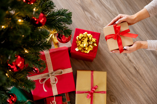 Close-up on a woman placing a gift under the Christmas tree - holiday season concepts