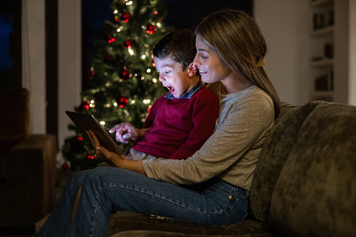 Mother and son at home watching a Christmas movie on a digital tablet and looking excited - holiday season concepts