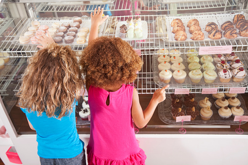 Multi-ethnic little girls (4-6 years) in bakery looking at cupcakes.