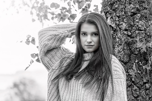 Black and white portrait of attractive long haired young woman dressed in a sweater posing outdoors.  Horizontally.