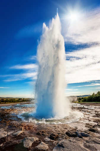 Geyser Strokkur against sun and blue summer sky, erupting hot water and steam. Iceland