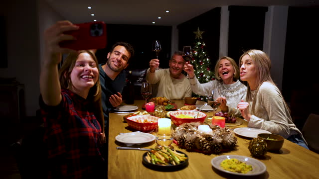 Happy teenage girl holding a smartphone while video calling someone during the family Christmas dinner all talking and smiling