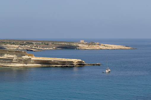 View on the beach, cliffs and lone motorboats by Il-Ħofra l-Kbira Bay in Malta