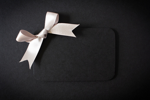 A black gift card with a silver bow on a black background, with copy space.