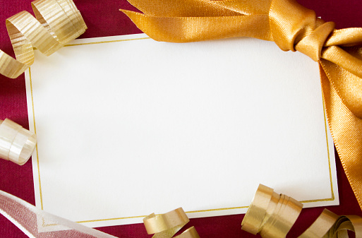 A blank card with gold and cream ribbons on a red background, with copy space.