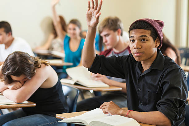 High Scool Students in Classroom A high school student raises his hand while others work on schoolwork in a classroom of diverse teen students. teenage high school girl raising hand during class stock pictures, royalty-free photos & images