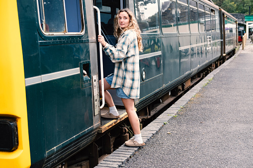 A young woman steps onboard a passanger train from a startion and platform, Tarka Valley Railway, Devon UK.