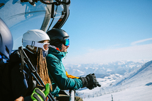 Group of snowboarders riding on the ski lift, getting up to the mountain peak.