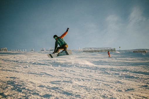 Male snowboarder riding in the sunset on a beautiful winter day, doing ride tricks.